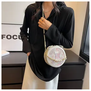 Détail d'un sac à bandoulière rond blanc avec chaîne en perles et texture tissée
