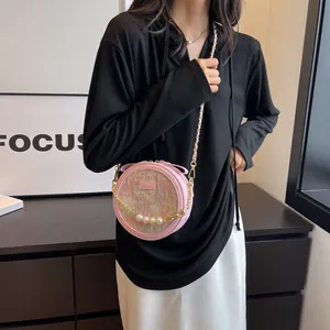 Sac bandoulière rond rose avec chaîne en perles et design texturé porté par un mannequin