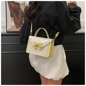 Detail of light yellow bow crossbody bag with wavy edge trim and brand logo