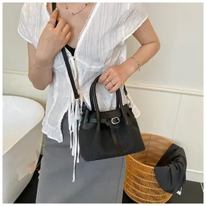 Detalle de bolso cubo negro con textura trenzada, hebilla plateada y correa bandolera