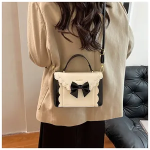 Rear view of a model carrying a cream and black bow-accented shoulder bag with wavy edges
