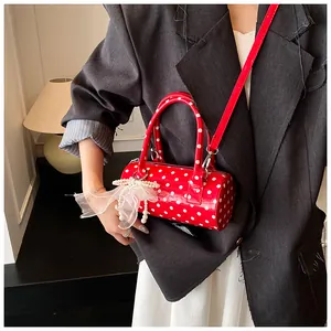 Detail einer roten Polka-Dot-Zylindertasche mit glänzendem Finish und Perlenanhänger