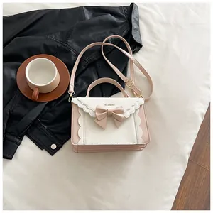 Detail of pink and beige crossbody bag with bow decoration and wavy trim on white fabric