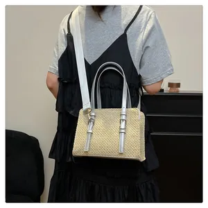 Detail of woven straw handbag showing silver handles and wide fabric shoulder strap