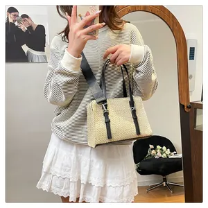 Detail of beige straw handbag with black leather straps and detachable shoulder strap