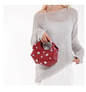 Detail of red glossy mini bag with silver rivets and bow accent held by a model