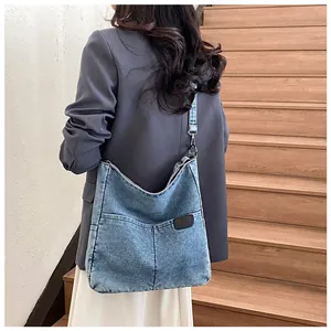 Detail of blue denim tote bag with leather tag, worn by model on wooden stairs