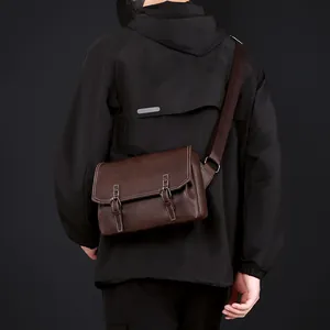 Close-up of brown PU leather messenger bag with pebble grain and contrast stitching detail