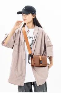 Detailed view of brown messenger bag with orange woven strap and secure black buckle