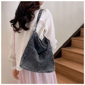Detail of grey denim tote bag showing side pocket and leather logo patch on a model