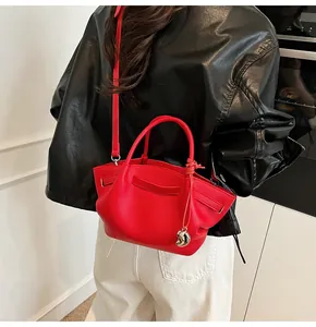 Detail of red leather tote bag with heart charm worn over a shiny black leather coat