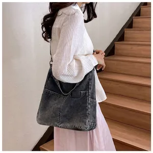 Detail of grey washed denim tote bag with side pocket and logo on model in daylight