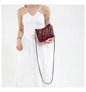 Detail of burgundy quilted crossbody bag with metal cross charm and skull hardware