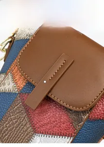 Detail einer bunten Patchwork-Ledertasche mit Zickzack-Nähten und goldenen Metallbeschlägen
