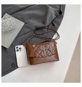 Detail of brown quilted crossbody bag with cross charm and punk style skull zipper