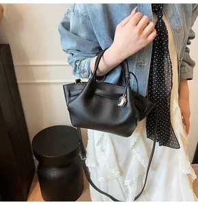 Detail of black lychee grain leather bucket bag with silver bean charm worn by model