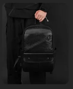 Detail of black leather backpack featuring slanted zipper and pocket with metal snap buttons