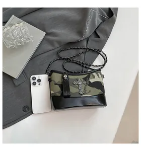 Detailed view of olive green camouflage and black leather crossbody bag with gothic hardware