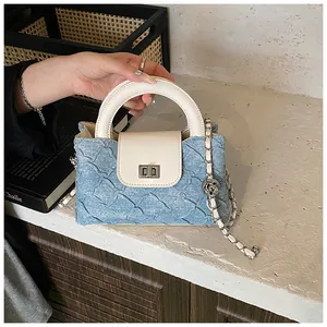 Detail der blauen Denim-Beuteltasche mit weißem Ledergriff und silberner Kugelkette