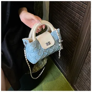 Detail der hellblauen Stepp-Eimertasche mit cremefarbenem Ledergriff und Silberkette