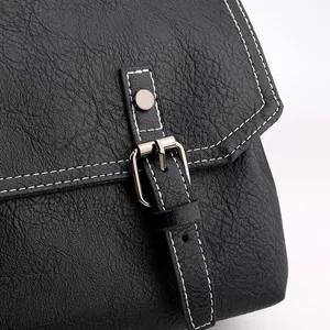 Detail of black lychee grain leather crossbody bag with white contrast stitching and buckle