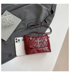 Macro shot of burgundy quilted bucket bag with gothic cross chain and phone for size reference