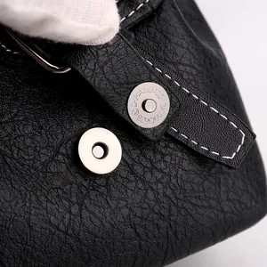 Macro shot of black pebbled leather bag flap with white contrast stitching and magnetic buckle