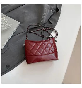 Detail of burgundy quilted leather hobo bag with silver chain strap on grey fabric