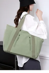 Dettaglio della borsa tote in nylon verde salvia con tasche a zip verticali indossata dal modello