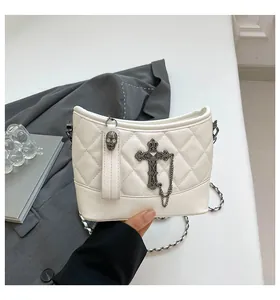 Macro detail of white quilted crossbody bag with metal cross and skull zipper charm