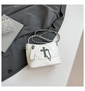 Close-up of quilted white crossbody bag with silver cross and skull charm detail