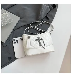 Detail of white quilted bucket bag with vintage cross charm and metal chain strap