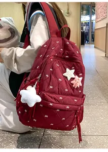 Detail of dark red quilted backpack with white bow prints and star-shaped charms