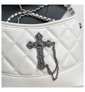 Detail of white quilted leather bag with gothic metal cross and woven chain strap