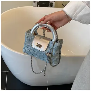 Detail der hellblauen gesteppten Denim-Beuteltasche mit silbernem Griff und Kettenriemen