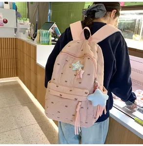 Detail of pink quilted backpack featuring embroidered bows and star pendants on straps
