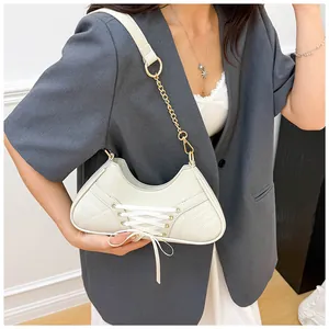 Detail of quilted creamy white bag featuring cross-lace ribbons and metal chain strap