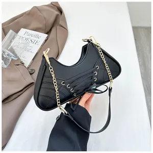 Detail of black leather underarm bag featuring decorative lacing and gold chain strap
