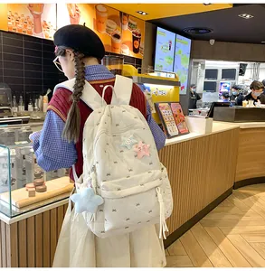 Detail of cream quilted backpack with bow embroidery and star charm in a cozy cafe setting