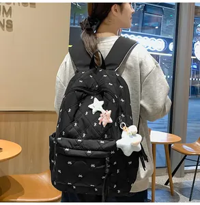 Detail of black quilted backpack with white bow patterns and plush star charm accessory