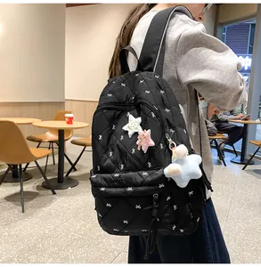 Detail of black quilted backpack with white bow patterns and plush star charms