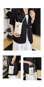 Detail view of cream-colored floral embroidery and orange flower charm on crossbody phone bag