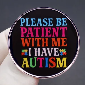 Badge autisme avec puzzle arc-en-ciel et texte Please Be Patient en émail noir