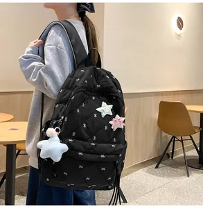 Close-up of black quilted backpack with white bow embroidery and star-shaped plush charms