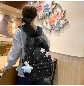 Detail of black quilted backpack featuring white bow embroidery and star plush pendant