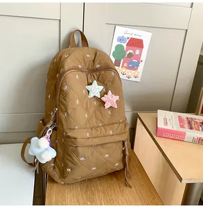Detail of brown quilted backpack with white bow embroidery and star charms on wood desk