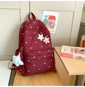 Detail view of wine red quilted backpack with white bow embroidery and star pendant charm