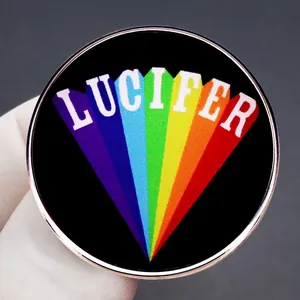 LUCIFER enamel pin with rainbow sunburst and gold finish held by white gloved fingers