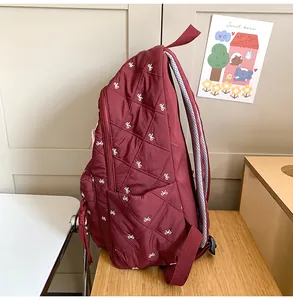 Detail of burgundy quilted backpack featuring white bow embroidery and side pocket