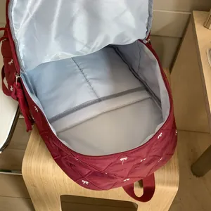 Red quilted nylon backpack with bow embroidery and interior pockets shown from top view